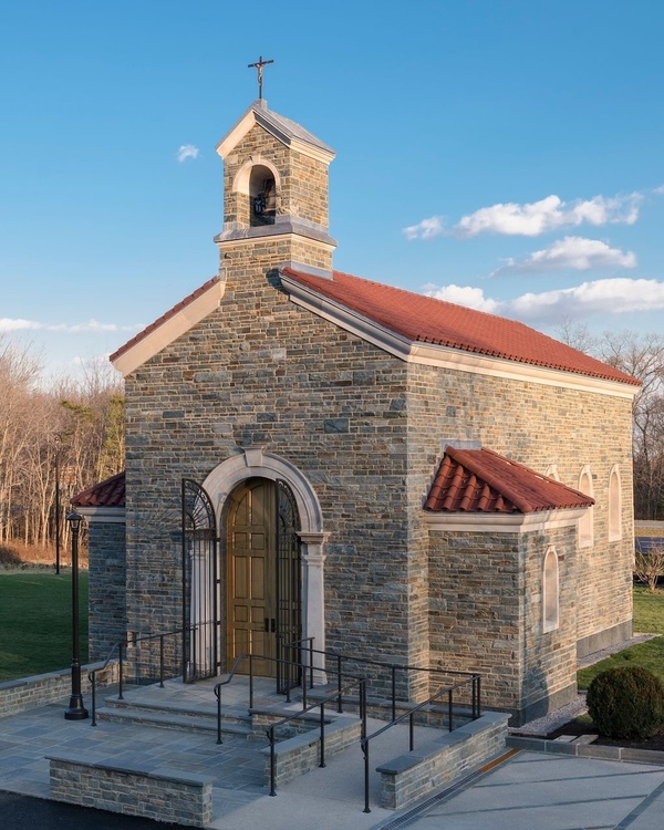 Picture of a modern-day chapel in a backyard. Stone building with bell tower with cross on top.