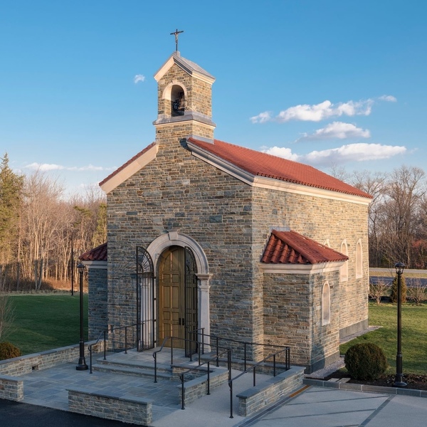 Picture of a modern-day chapel in a backyard. Stone building with bell tower with cross on top.