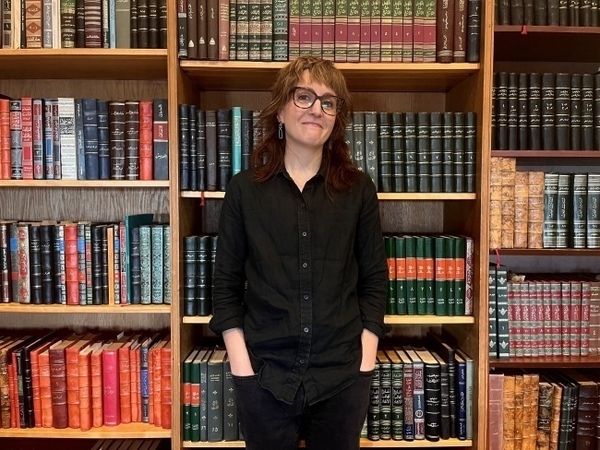 A woman stands in front of a series of bookshelves full of books