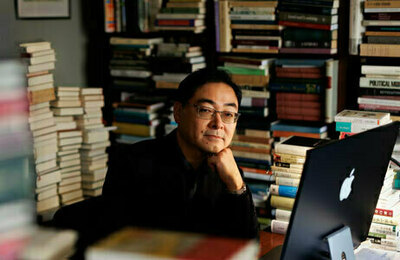 Man sitting in office at a computer, surrounded by books